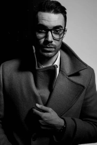 身穿长大衣 头戴眼镜 手握食指 穿着黑色灰色背景服装的优雅年轻人 — 图库照片