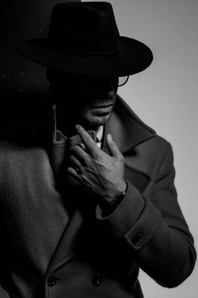 長いコートを着た謎のエレガントな男帽子と眼鏡をかけ指を下に向け黒い灰色の背景の影の中に立って — ストック写真