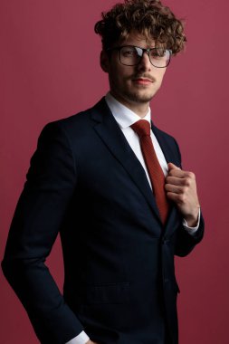 Yakışıklı, zarif iş adamı bir eli cebinde, ceketini tamir ediyor ve pembe stüdyonun arka planındaki kameraya bakıyor.