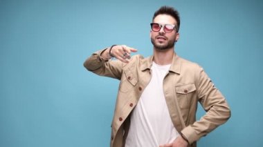 Mutlu genç adam el ele verip düşünüyor ve hatırlamaya çalışıyor, parmaklarını gösterip alkışlıyor, gülüyor ve mavi arka planda hareket ediyor.