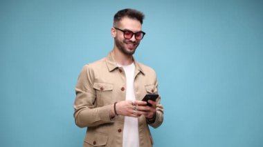 Ceketli, gözlüklü, yukarı aşağı bakan, e-postaları okuyan, yumruğunu kaldırıp mavi arka planda zafere tezahürat eden mutlu genç manken.