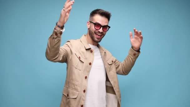 幸せな若いカジュアルな男はジャケットを着て笑って動き腕を揺らし青い背景で勝利を祝う — ストック動画