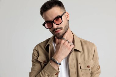 Ceketli, güneş gözlüklü, el ele tutuşan ve gri arka planda poz veren mutlu genç bir adam.