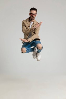 Ceketli, güneş gözlüğü takan, el ele tutuşup moda pozu veren ve gri arka planda poz veren havalı bir genç.