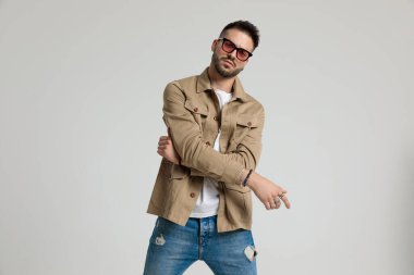 Ceketli, güneş gözlüğü takan havalı bir adam. Modaya uygun bir şekilde el ele tutuşup poz vermek, gri arka planda durmak.