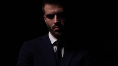 Moda ışığında durup poz veren, sessiz hareketler yapan, çeneye dokunan ve düşünen, kravat takan ve arka planda poz veren genç, zarif bir manken.
