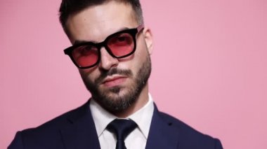 Bir moda işadamının baştan çıkarıcı bir bakışla kameraya bakıp pembe arka planda gülümsemesini.