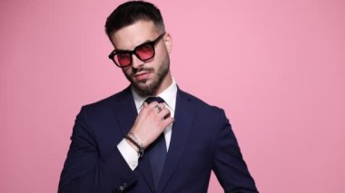 Genç ve seksi manken, sıkı bir tavırla kravatını ve ceketini düzeltiyor, kollarını kavuşturup, pembe arka planda kahkahalarla gülüyor.