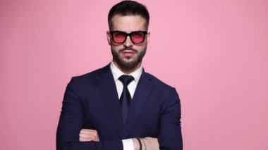 Yakışıklı maço işadamı kollarını kavuşturup güneş gözlüğünü çekiyor ve onlara bakıyor ve pembe arka planda sert bir tavır sergiliyor.