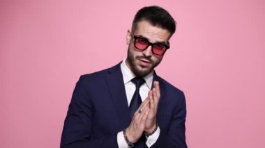 Seksi, baştan çıkarıcı iş adamı ellerini ovuşturuyor, aşağı bakıyor, yana bakıyor, boynunu okşuyor, parmaklarını şaklatıyor ve pembe arka planda yolunu buluyor.