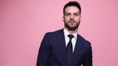 Baştan çıkarıcı maço işadamı kravatını düzeltiyor, ceketini düzeltiyor, yana dönüyor ve ellerini ovalıyor sonra pembe arka planda kameraya sırtını dönüyor.
