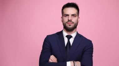 Davranışları olan seksi iş adamı elini göğsüne uzatıyor, elini sakalına uzatıyor ve pembe arka planda gururla omzunu temizliyor.