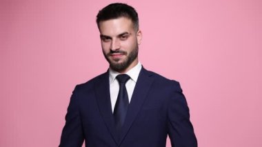 Çekici iş adamı bir taraftan diğer tarafa dönüyor, etrafına bakıyor, dans ediyor ve yumruklarını pembe arka planda hareket ettiriyor.