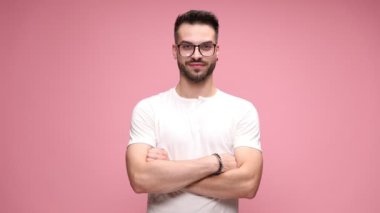 Kolları katlanmış, gözlüklü, kameraya bakıp gülümseyen ve pembe arka planda gülümseyen genç moda gündelikçisi.