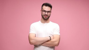 Çekici, gözlüklü, kolları çapraz duran, kameraya bakıp gülümseyen ve iki eli pembe arka planda olan bir adam.