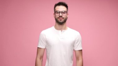 Gözlüklü yakışıklı, pembe arka planda duran, kollarını göğsüne bağlayan ve gülümseyen bir adam.