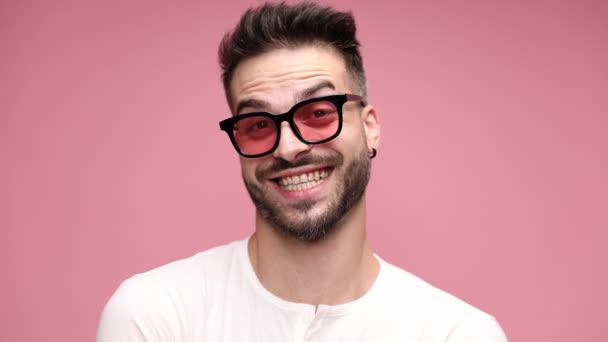 若いハンサムなカジュアルな男が笑顔で大声で笑ってピンクの背景にサングラスをかけて — ストック動画