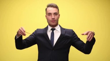 Takım elbiseli zarif genç işadamı elinde kondüktör copu tutuyor ve orkestra yönetiyor, senfoniyi koordine ediyor, sarı arka planda hareket ediyor ve el kol hareketi yapıyor.