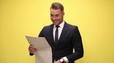Şok olmuş genç işadamı, huzurlu bir gazete okuyor, şok edici bir şekilde ağzını açıyor, avuçlarını içine alıyor, başını sallıyor ve sarı arka planda onaylamıyor.