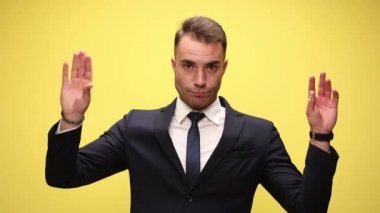 Takım elbiseli genç adam kollarını havaya kaldırıyor ve sarı arka planda konuşan eller yapıyor.