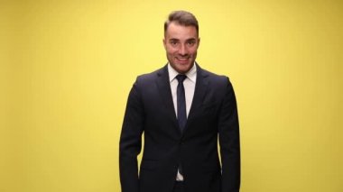 Takım elbiseli genç işadamı yukarı bakıyor, kaşlarını kaldırıyor ve gülümsüyor, yumruklarını havaya kaldırıyor, bağırıyor ve sarı arka planda zaferi kutluyor.
