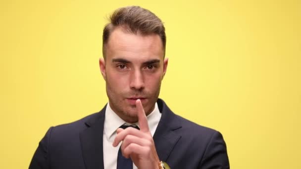 セクシーなエレガントなビジネスマンでスーツを保持指に口と作る沈黙ジェスチャー上の黄色の背景 — ストック動画