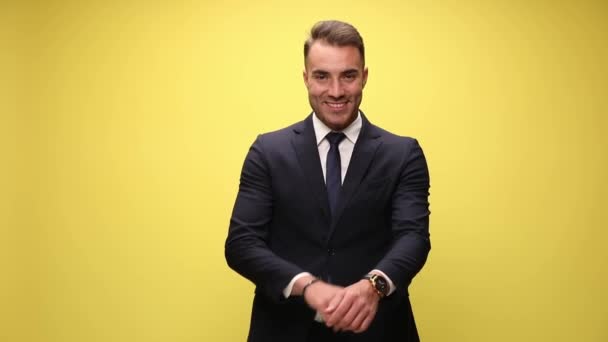 スーツ姿のセクシーな若いビジネスマンが笑顔で腕を交差させ手を顔に手をつないでひげとあごに触れ黄色の背景に立って — ストック動画