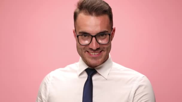 エレガントな若い男です白いシャツに身を包んだ眼鏡笑顔とピンクの背景に貯金箱を示す — ストック動画