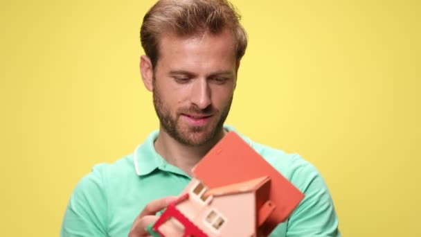 興奮した若い男が家を持って推薦し 空中で拳を握り 黄色の背景で勝利を祝う — ストック動画