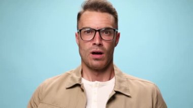 Yakışıklı sıradan bir adam iğreniyor, şaşırıyor, kızgın ve kafasına dokunuyor, çığlık atıyor ve mavi arka plandaki kameraya yumruklarını gösteriyor.