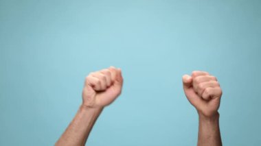 İki yumruk sallıyor, tamam işareti yapıyor, kameraya bakıyor ve mavi arka plandaki başarıları kutluyor.