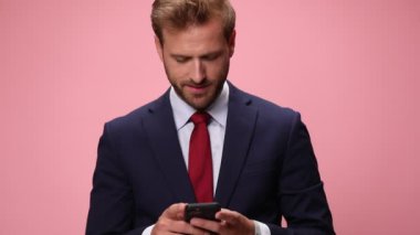 Mutlu zarif moda adamı telefonu tutuyor, e-postaları okuyor, pembe arka planda mesajlaşıyor ve gülümsüyor.