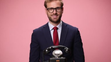 Lacivert takım elbiseli gülümseyen genç bir işadamı. Gözlüklü. Telefonlara cevap veren, gülen ve pembe arka planda başparmak hareketi yapan.