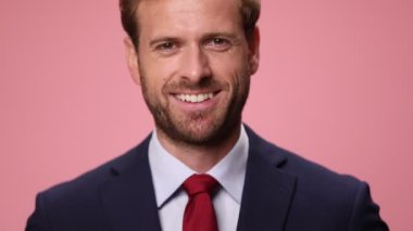 Pembe arka planda gülümseyen ve kollarını kavuşturan lacivert takım elbiseli zarif genç adama yaklaş.