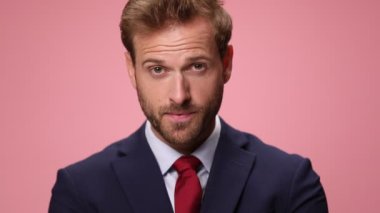 Donanma mavisi takımlı mutlu genç adam yukarı bakıyor, gülümsüyor ve pembe arka planı işaret ediyor.