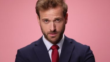 Lacivert takım elbiseli şık moda adamına yaklaş, yukarı bak, baş parmak işareti yap ve pembe arka planda gülümse.