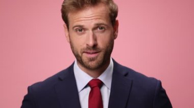 Donanma mavisi takımlı zarif mutlu adamın yakın plan fotoğrafını çek. Gülümse, parmaklarını göster ve pembe arka planda telefon hareketi yap.