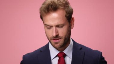 Baştan çıkarıcı, lacivert takım elbiseli genç iş adamı yukarı bakıyor, gülümsüyor, kaşlarını kaldırıyor, pembe arka planda flört ediyor.