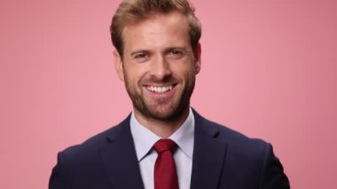Lacivert takım elbiseli genç işadamı elinde anahtarlarla ev modelini gösteriyor, pembe arka planda gülümsüyor.
