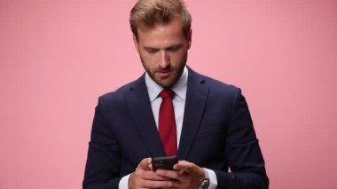 Elinde telefon tutan, mesajlar okuyan, düşünen, yumruğunu kaldırıp pembe arka planda kutlama yapan lacivert takımlı zarif bir adam.