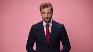 Lacivert takımlı zarif genç yukarı bakıyor, başparmağına ve işaret parmağına dokunuyor ve iyi bir jest yapıyor, pembe arka planda gülümsüyor.