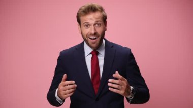 Mutlu, lacivert takımlı, ağzı açık, ağzı açık, ağzı açık, yumruklarını havaya kaldırmış, kutlama yapıyor, çığlık atıyor ve pembe arka planda gülüyor.