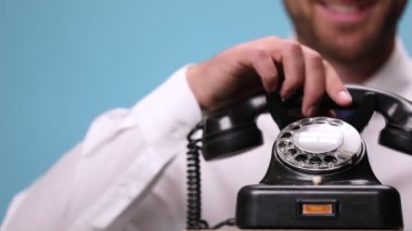 Konuşan, gülen, telefonu kapatan ve mavi arka plandaki kamerayı işaret eden bir işadamı tarafından cevaplanan eski bir telefonu kapatın.