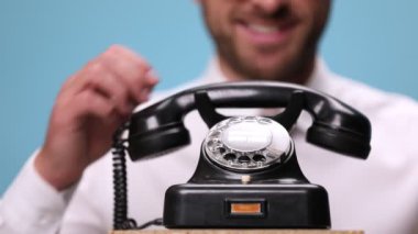 Yakışıklı bir işadamının cevapladığı eski bir telefonu kapatıyorum. Konuşuyor, gülüyor, telefonu kapatıyor ve mavi arka plandaki kamerayı işaret ediyor.