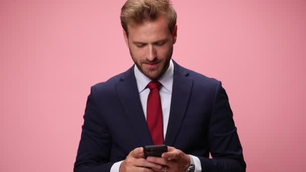 ネイビーブルーのスーツを着た幸せな若いビジネスマンがメールを読んだり笑顔で空中で拳を握りピンクの背景で祝う — ストック動画