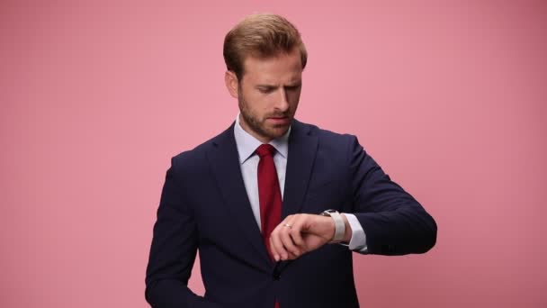 ネイビーブルーのスーツを着たエレガントなビジネスマンが時間をチェックし うなずき 同意しない 指の警告ジェスチャーとスコアリングを作り 指を頭に向け ピンクの背景に時間を示す — ストック動画