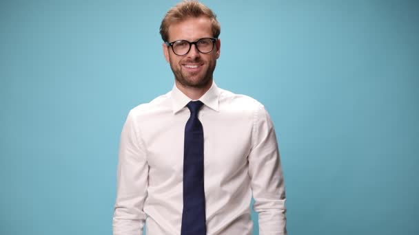 性感的生意人 戴着眼镜 脸上挂着笑容 一只手插在口袋里 用蓝色背景的相机对着他 — 图库视频影像