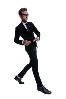 Siyah takım elbiseli zarif genç adam beyaz arka planda güvenle yürümeye çalışıyor.