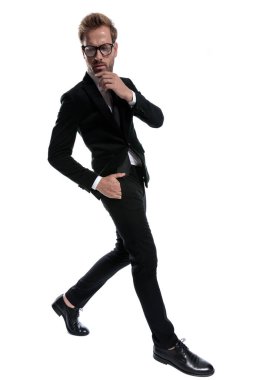 Siyah takım elbiseli dalgın bir işadamı beyaz arka planda tek başına yürürken, kıt kanaat geçiniyor.