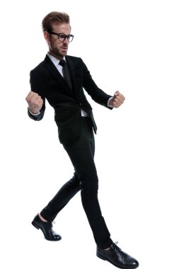 Siyah takım elbiseli şık havalı bir adam yumruklarını kaldırıyor, kutluyor, beyaz arka planda tek başına yürüyor, tüm vücuduyla.